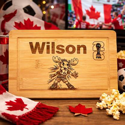 Wooden cutting board with engraved design and text, surrounded by sports-themed decor including a soccer ball and Canadian flag.