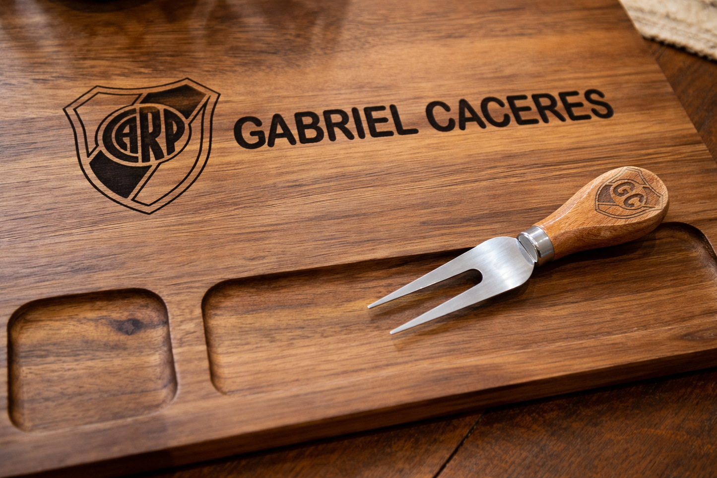Wooden cutting board with engraved name and logo, accompanied by a wooden-handled fork.
