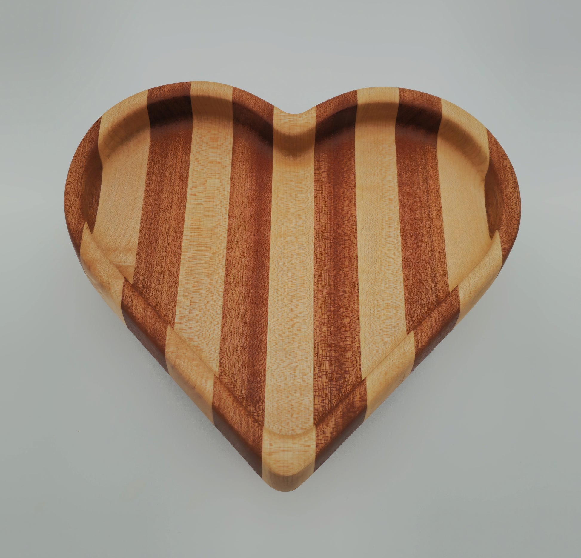 Heart-shaped wooden cutting board with striped pattern on a light gray background