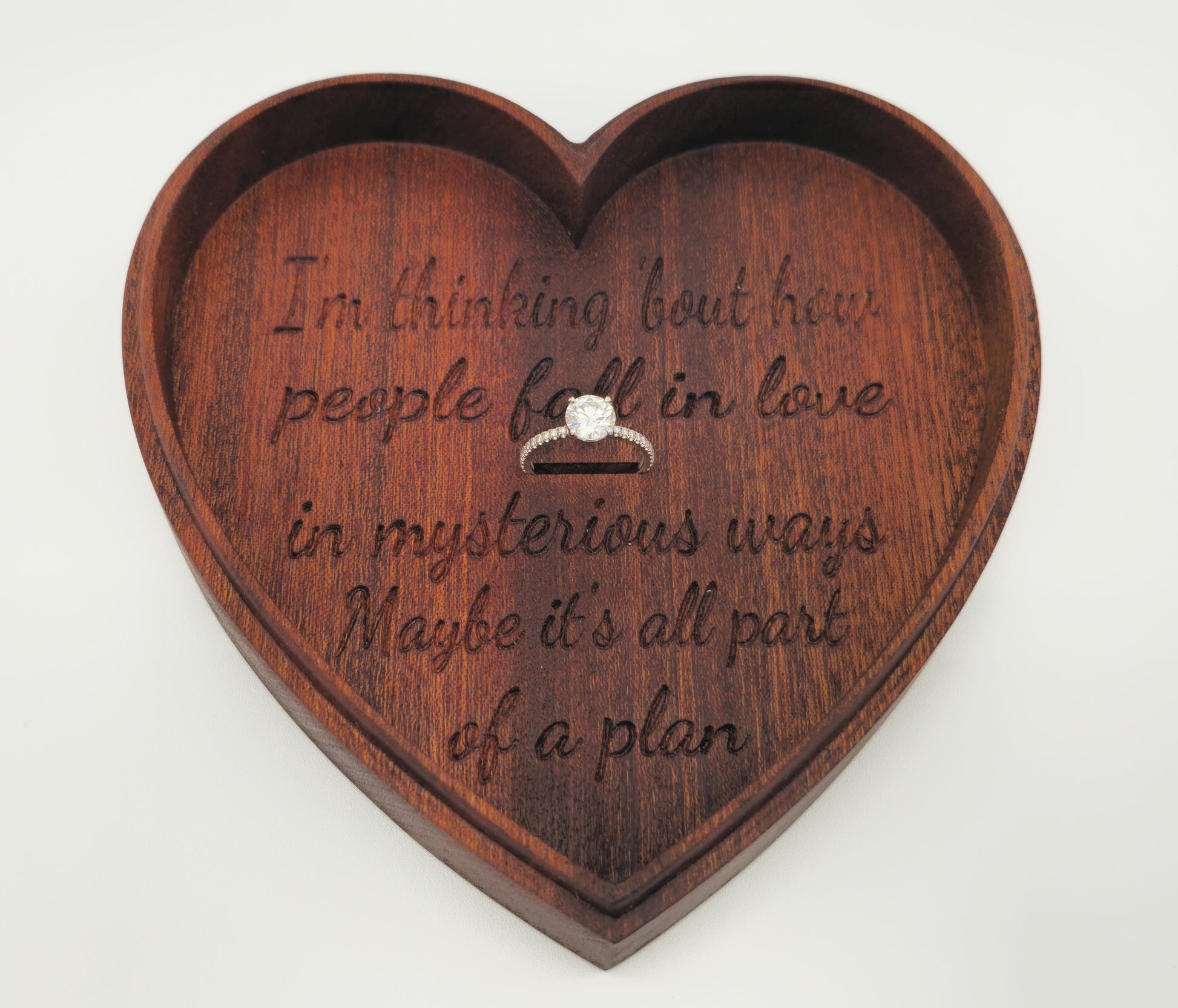 Heart-shaped wooden box with engraved text and a ring inside on a white background