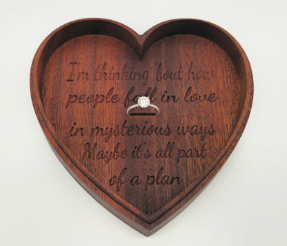 Heart-shaped wooden box with engraved text and a ring inside on a white background