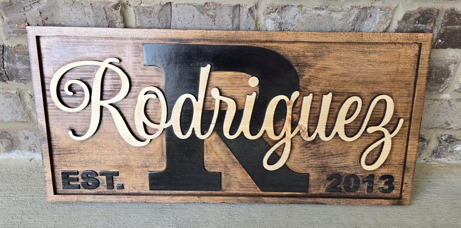 Wooden sign with 'Rodriguez' and 'R' design against a brick wall background